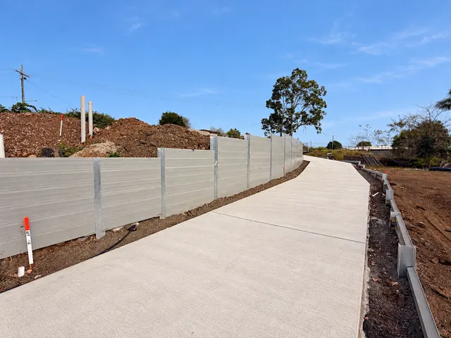 Curving concrete access path alongside a grey sleeper retaining wall
