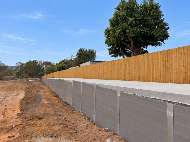 Grey sleeper retaining wall with a timber boundary fence above a concrete path