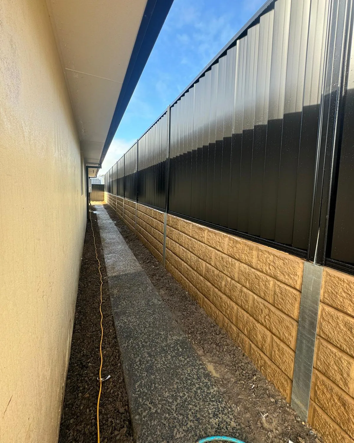 Black Colorbond fencing above sandstone-finish concrete sleepers
