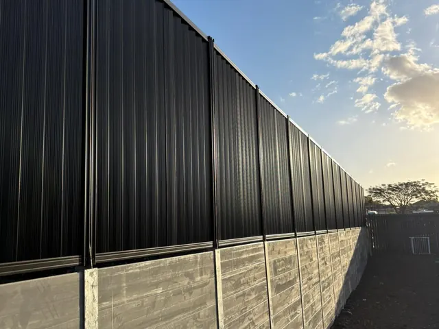 Black Colorbond boundary fencing above a light textured sleeper retaining wall
