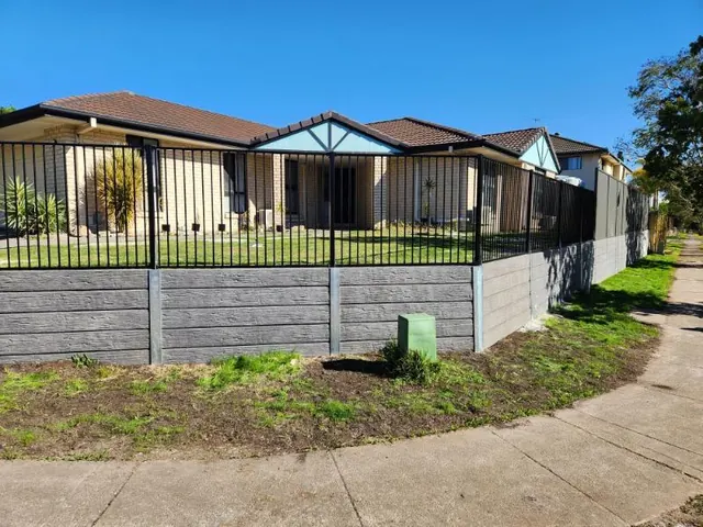 Low sleeper retaining wall and black metal fencing around a front lawn