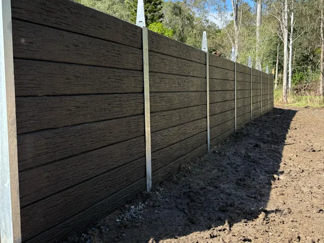 Dark timber-look sleeper wall along a garden boundary with established trees
