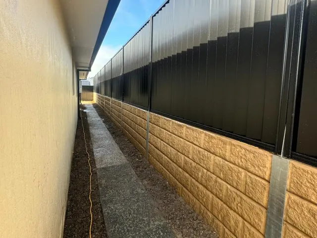 Black Colorbond fencing over sandstone-look sleepers along a home side path