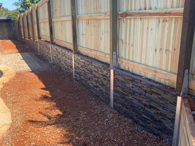 Timber boundary fence above a textured sleeper wall beside a paved patio