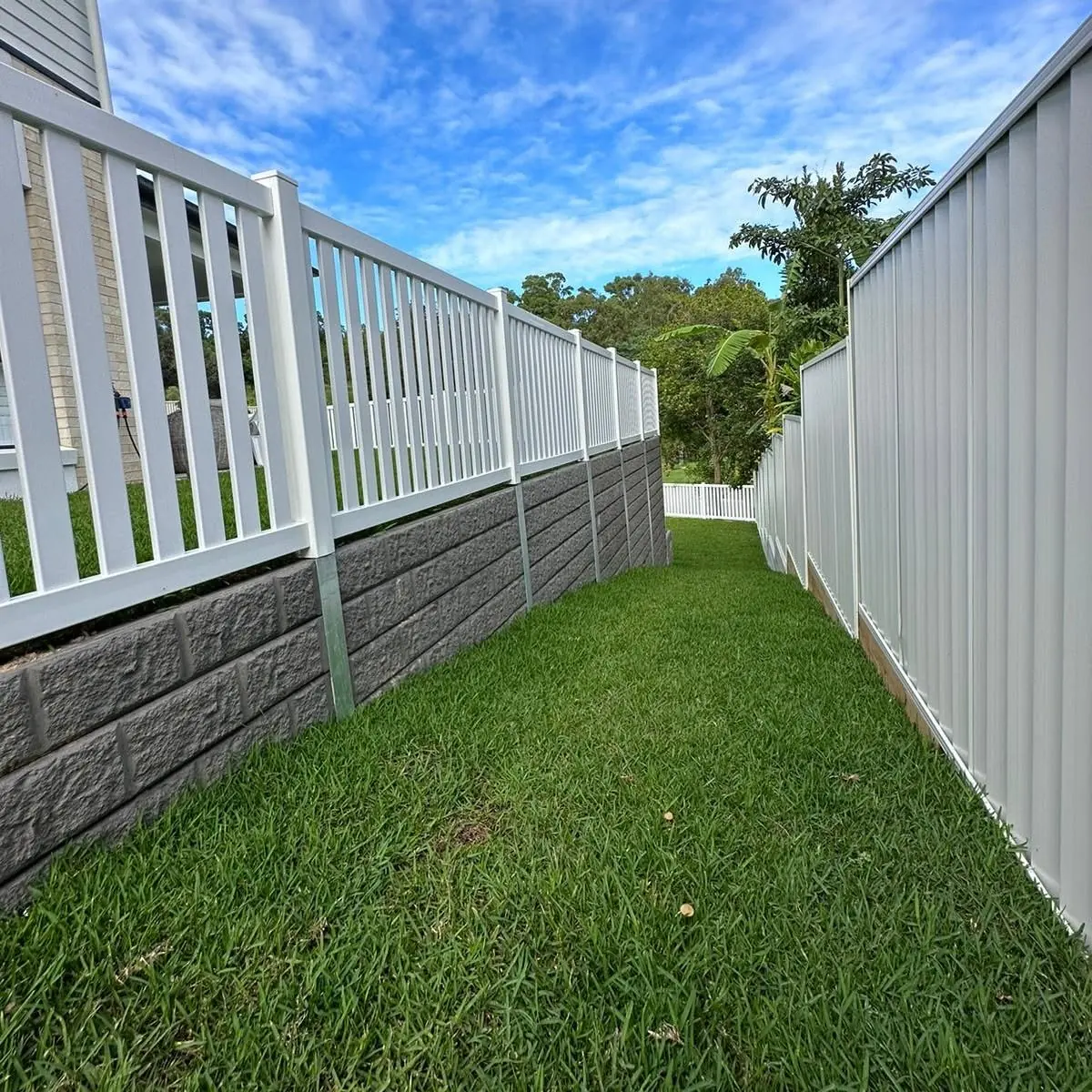 Textured sleeper retaining wall with white balustrade alongside a residential lawn